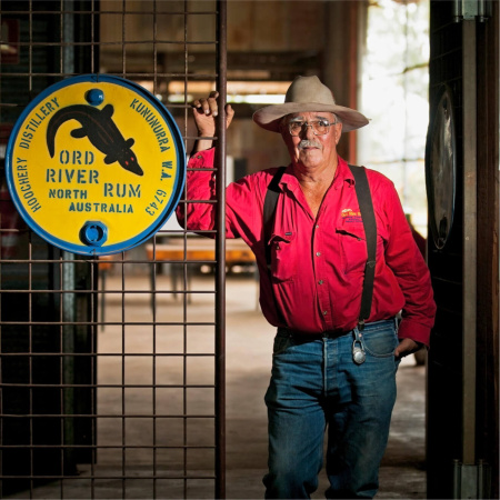 Raymond “Spike” Dessert III at te Hoochery Distillery, standing next to a hand painted sign